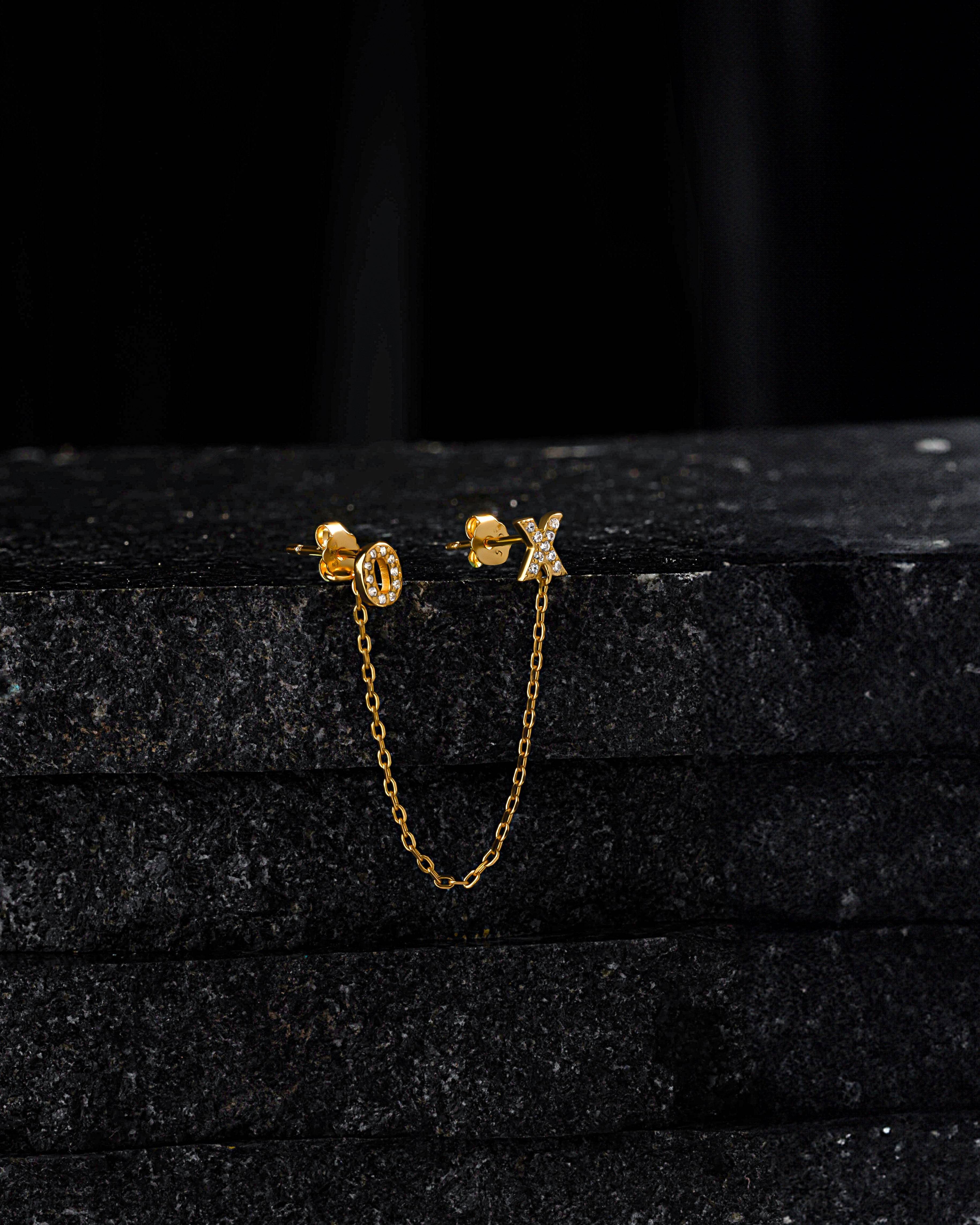XO - Create 3 Chain Connector Earring displayed on black stone, showcasing gold chain and crystal-studded X and O studs for versatile styling.