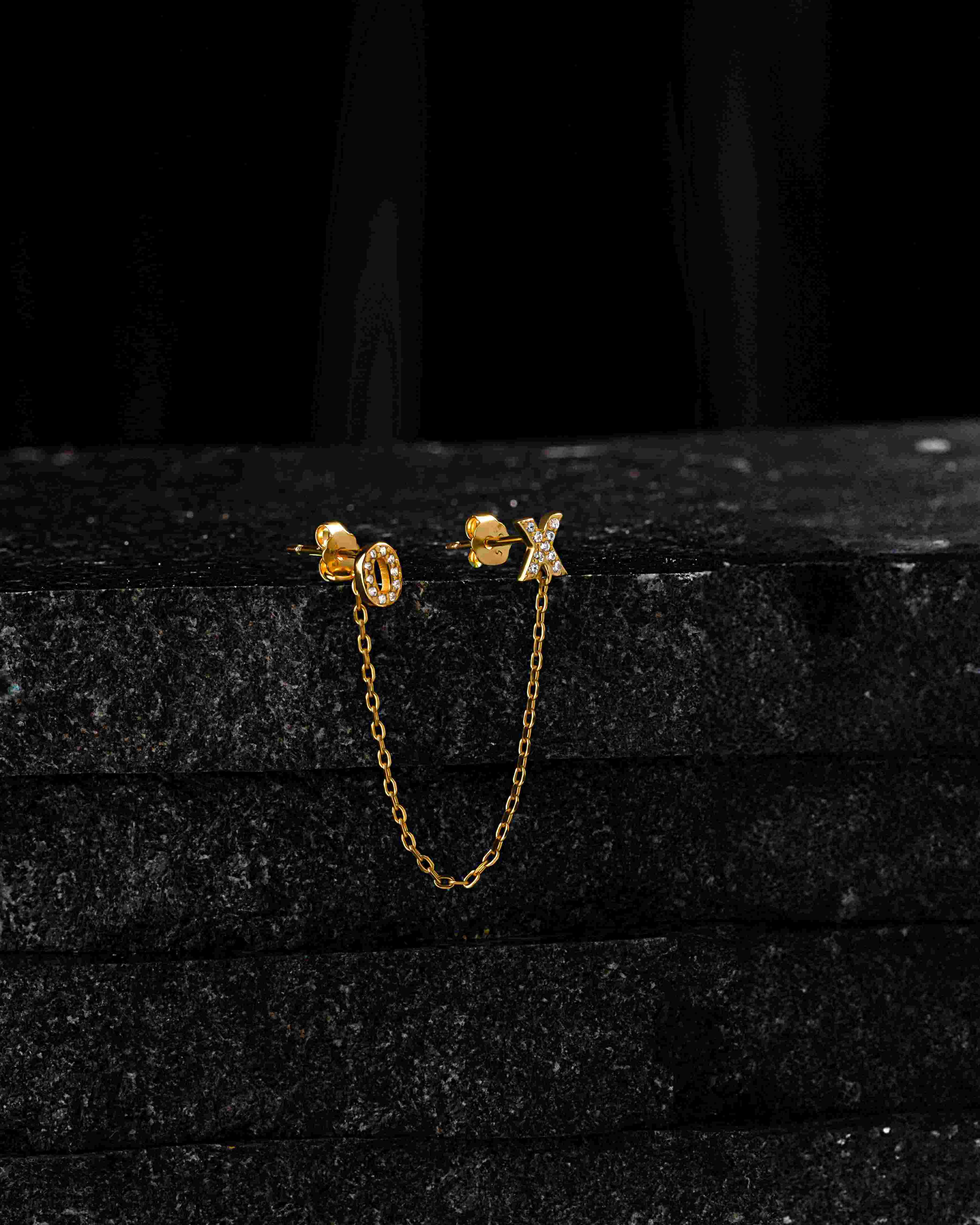 Gold XO 3 in 1 chain connector earring with pavé O and X studs displayed on black stone, highlighting its elegant, versatile design.