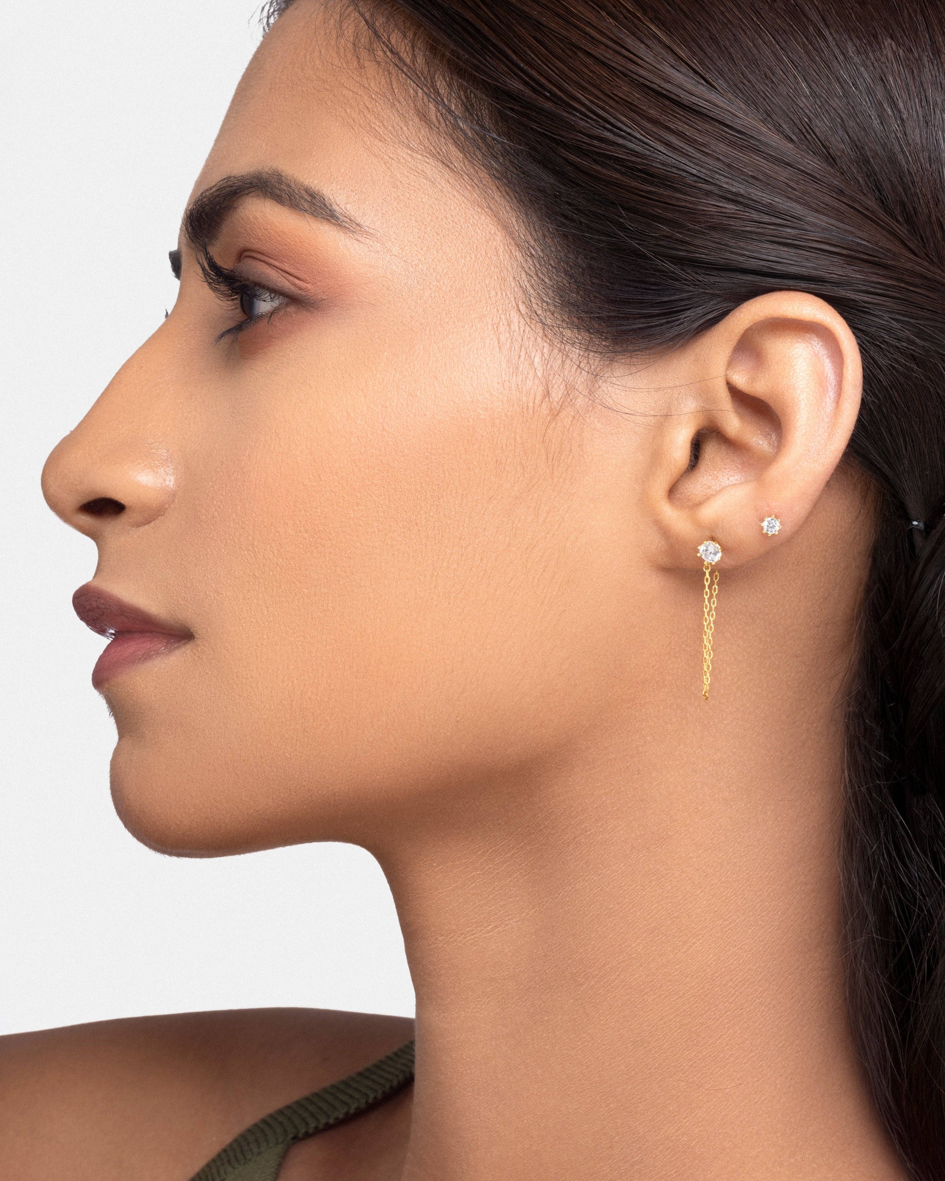 Model wearing the Solitaire Chain Connector - 3-in-1 stud on the ear, showcasing its elegant dual-stud design with a connecting gold chain.
