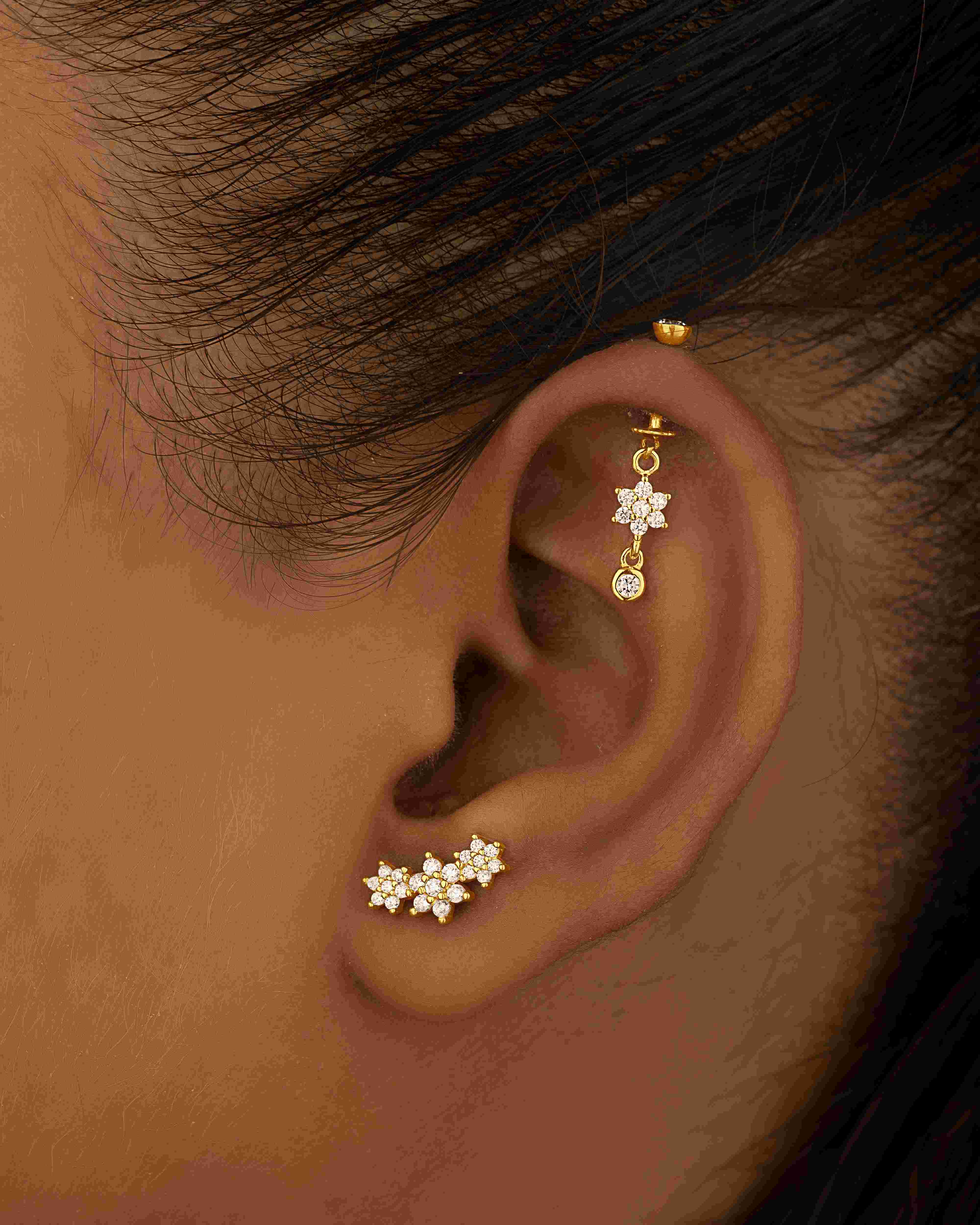 Model wearing elegant zircon drop helix piercing earring with five-petal flower design. Stylish gold-tone charm adds sparkle to helix ear piercing.